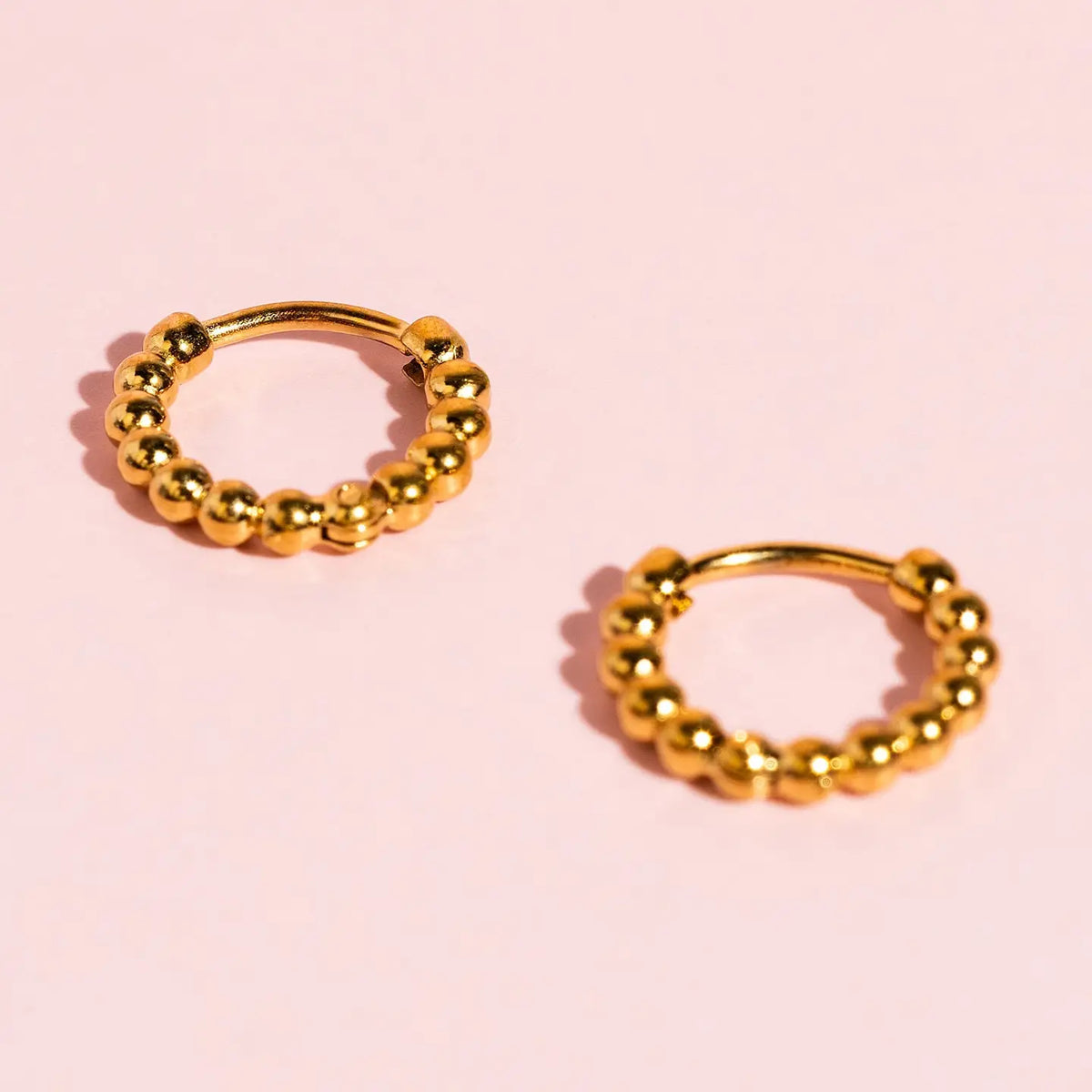 Gold tiny dot huggies earrings hypoallergenic, plated, pierced. Pierced Co. Tiny Dot Huggies flat lay