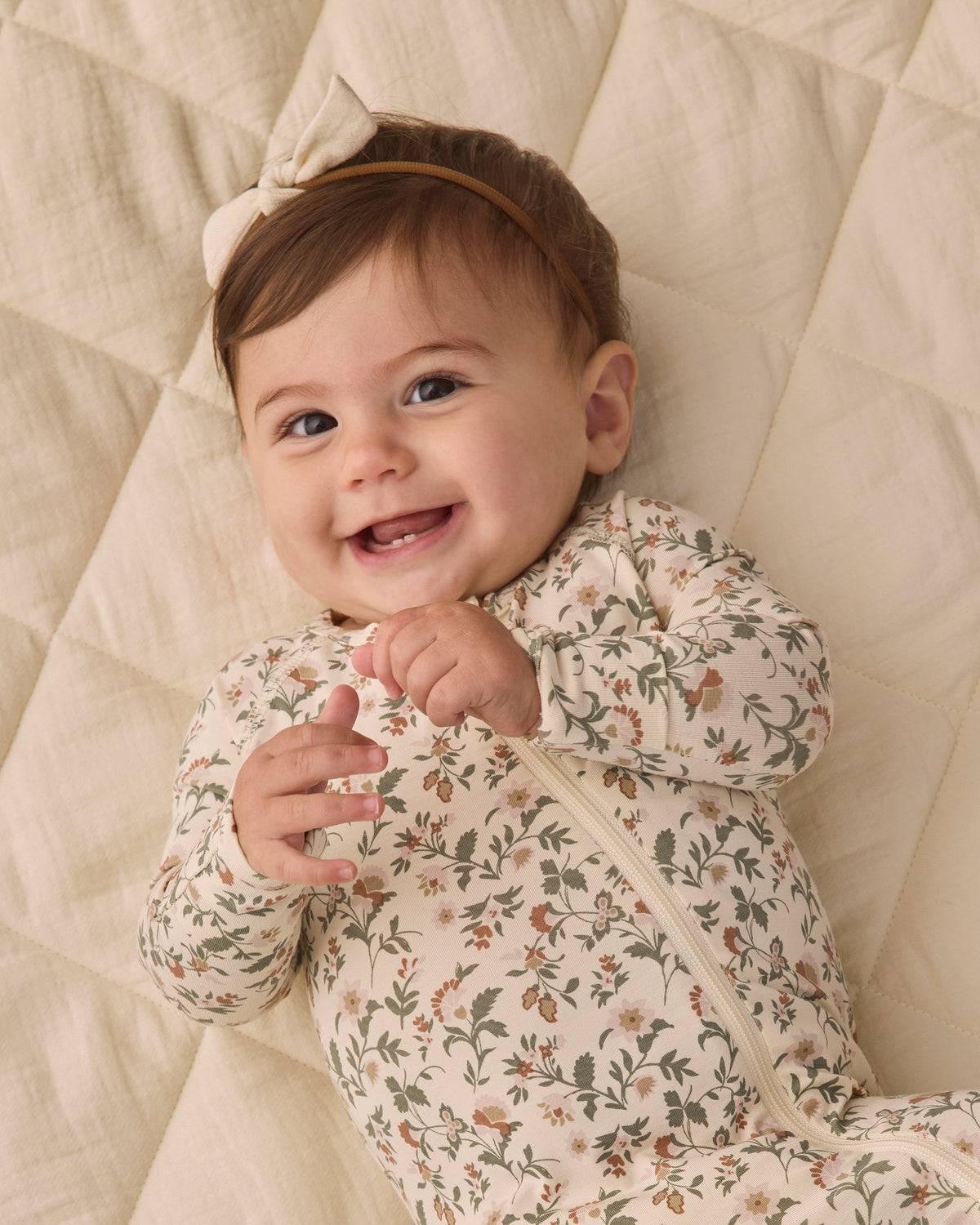 Smiling baby girl wearing Quincy Mae Baby Bamboo Zip Footie in Holiday Floral close up portrait