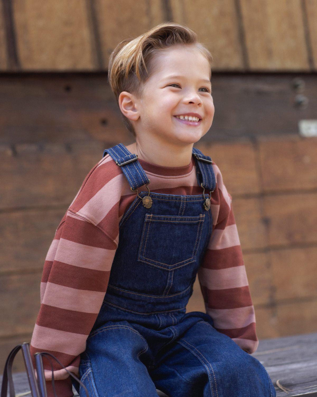 Young boy modeling the Rylee + Cru Oversized Sweatshirt | Brick + Clay Stripe paired with overalls