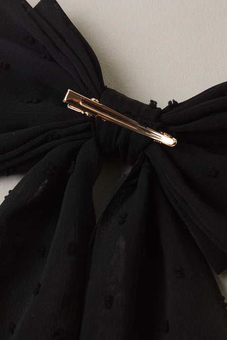 A close-up of the Noralee Alice Bow | Black, held in the center by a metallic hair clip against a light gray background.