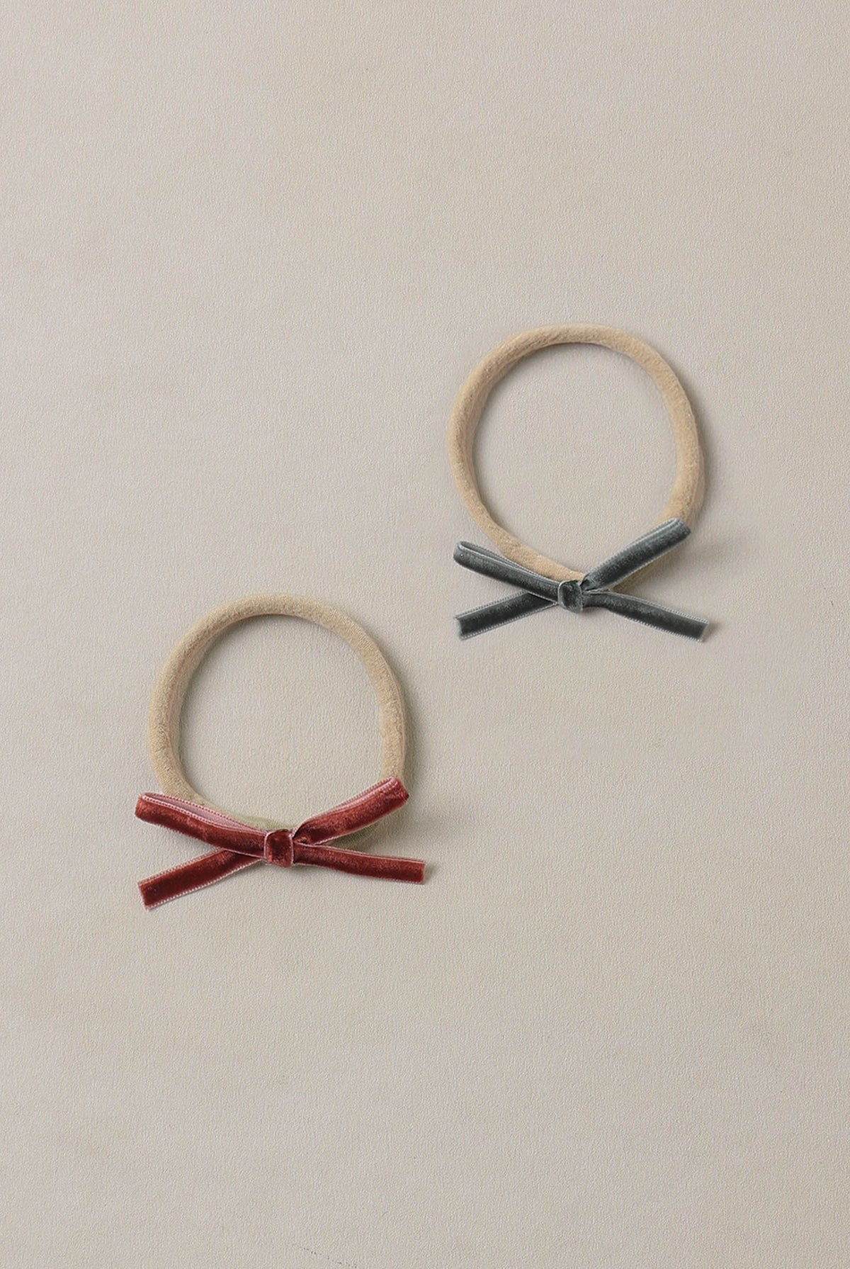 Two beige headbands with bow details on a beige background. Noralee headband in Green and Ruby
