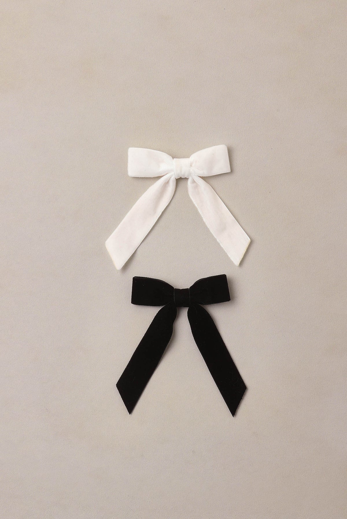 Two velvet bows, one white and one black, on a beige background. The Noralee Velvet Bows Set in Black and Ivory