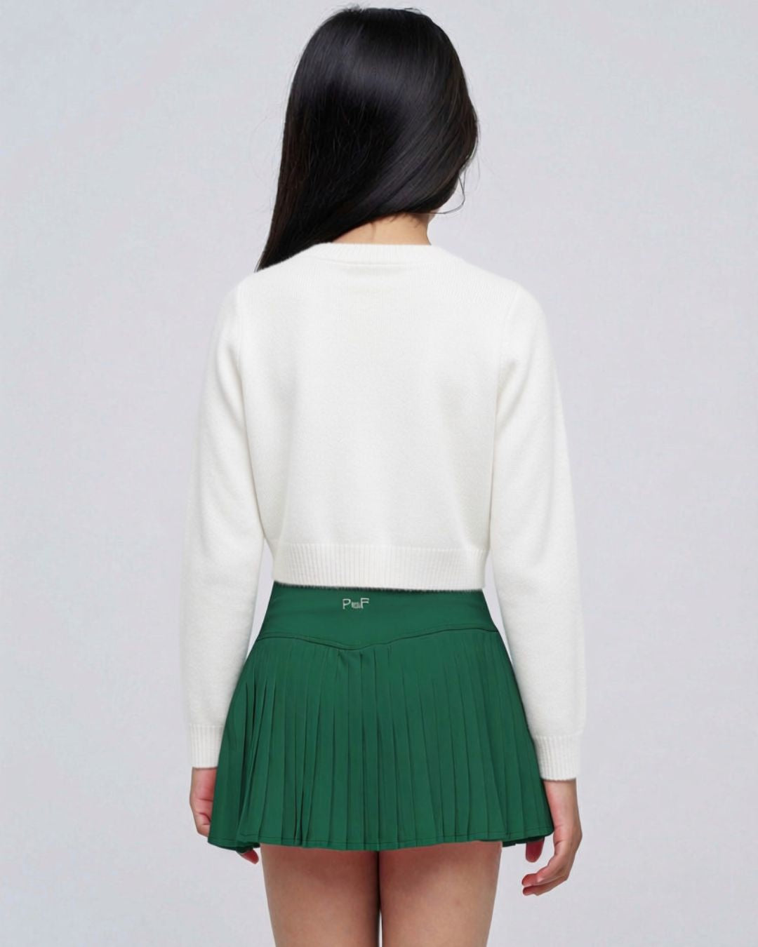 Parfum de Fit Pleated Mini Skirt Evergreen Noir on model with white sweater pose from back