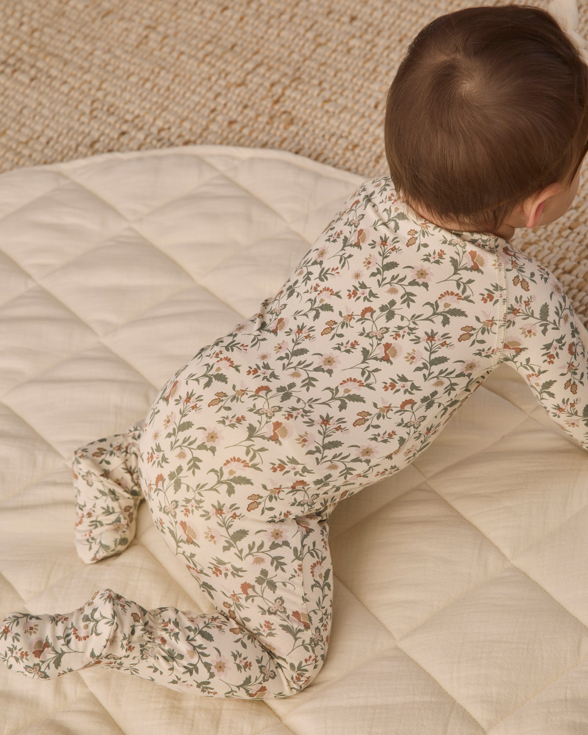 Back to camera angle baby model wearing Quincy Mae Baby Bamboo Zip Footie in Holiday Floral 