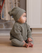 Infant model wearing Quincy Mae Baby Luca Pant in Spruce, Quincy Mae Chunky Knit Baby Sweater in Spruce, and Quincy Mae Beanie in Spruce side view photo