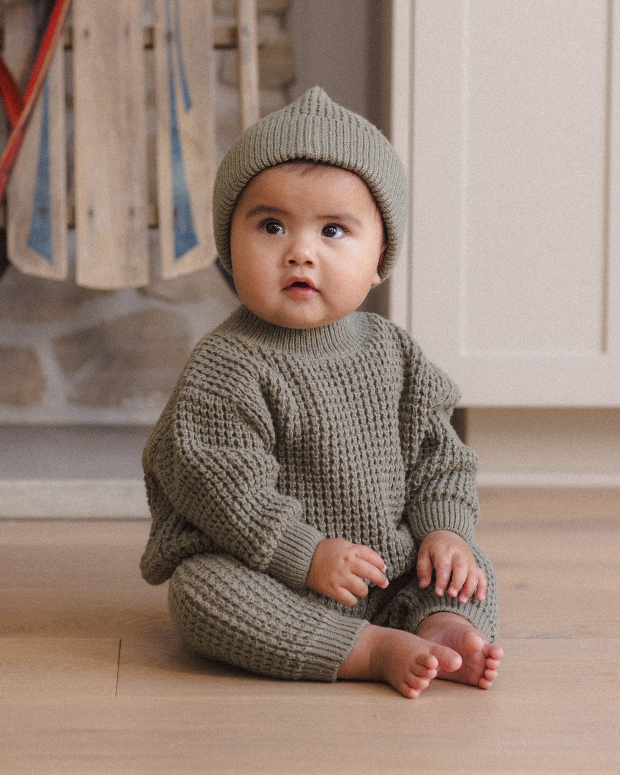 Infant model wearing Quincy Mae Baby Luca Pant in Spruce and Quincy Mae Chunky Knit Baby Sweater in Spruce and Quincy Mae Beanie in Spruce lifestyle photo