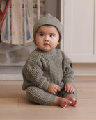 Infant model wearing Quincy Mae Baby Luca Pant in Spruce and Quincy Mae Chunky Knit Baby Sweater in Spruce and Quincy Mae Beanie in Spruce lifestyle photo