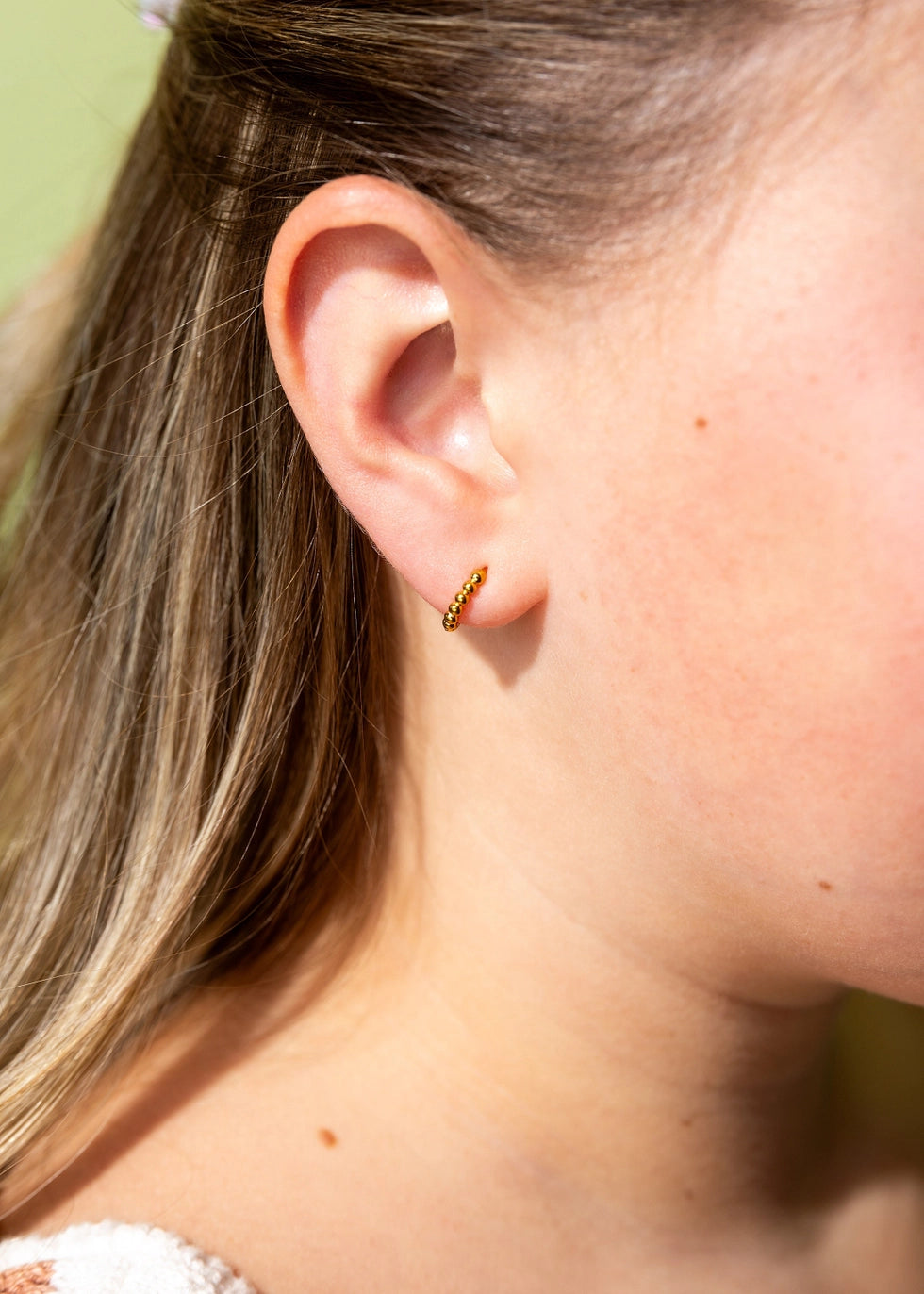 Pierced Co. Tiny Dot Huggies flat lay earring on model close up