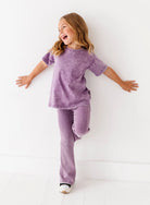 Child wearing a purple outfit standing against a white background