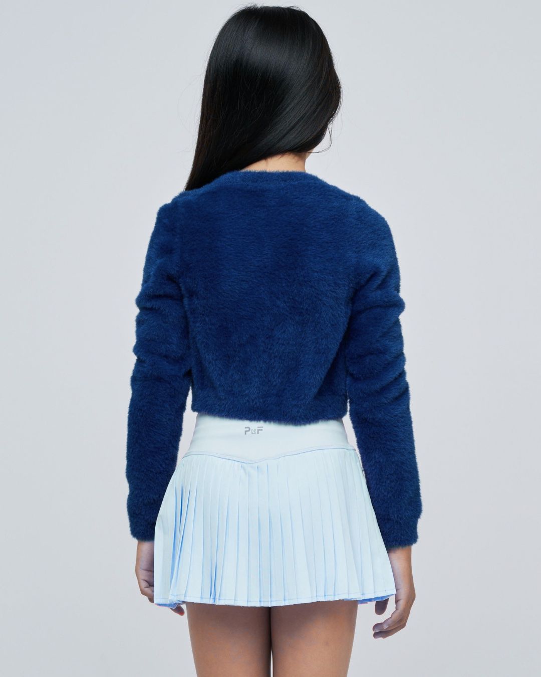 Parfume de fit pleated tennis skirt frost on model back pose paired with dark blue fuzzy sweater