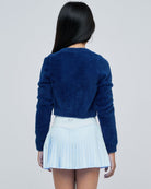 Parfume de fit pleated tennis skirt frost on model back pose paired with dark blue fuzzy sweater
